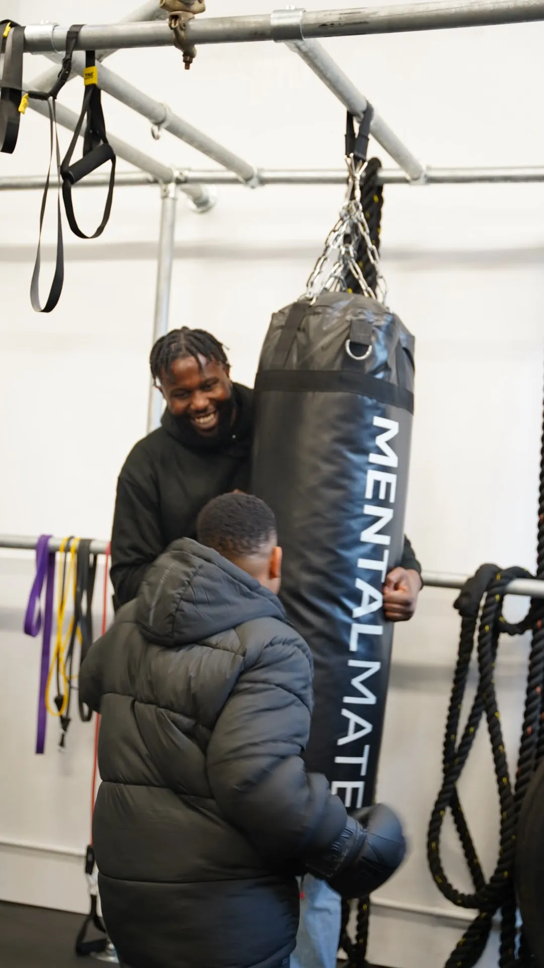 A Care Cove coach smiling as they hold a punch bag for a young person wearing boxing gloves